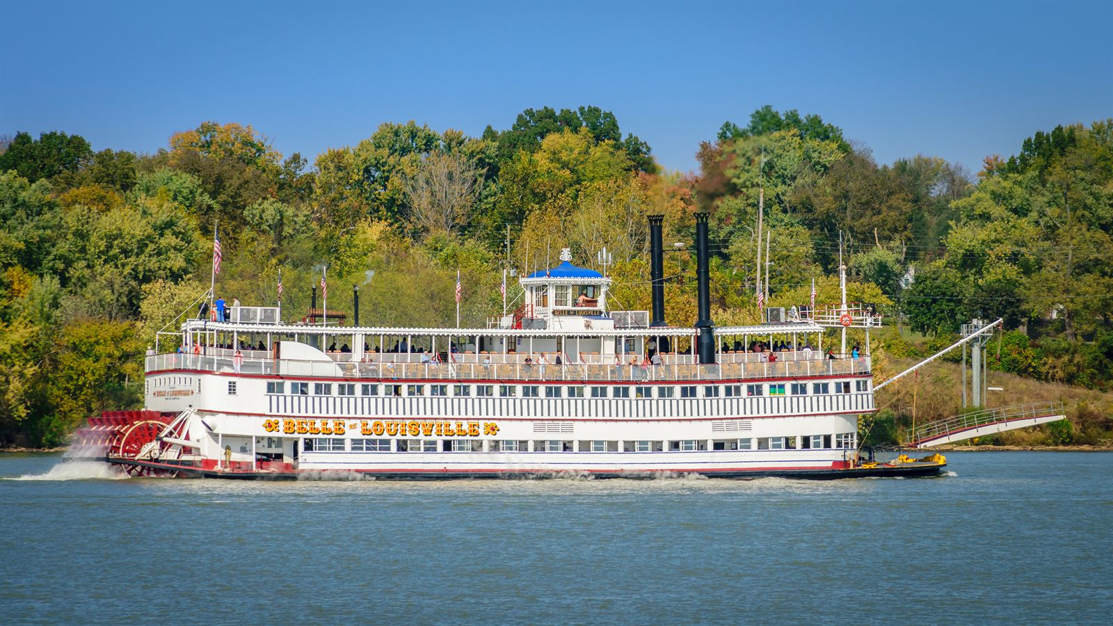 The Belle of Louisville, a 1914 steamboat still offering steamboat cruises, passing wooded banks in autumn